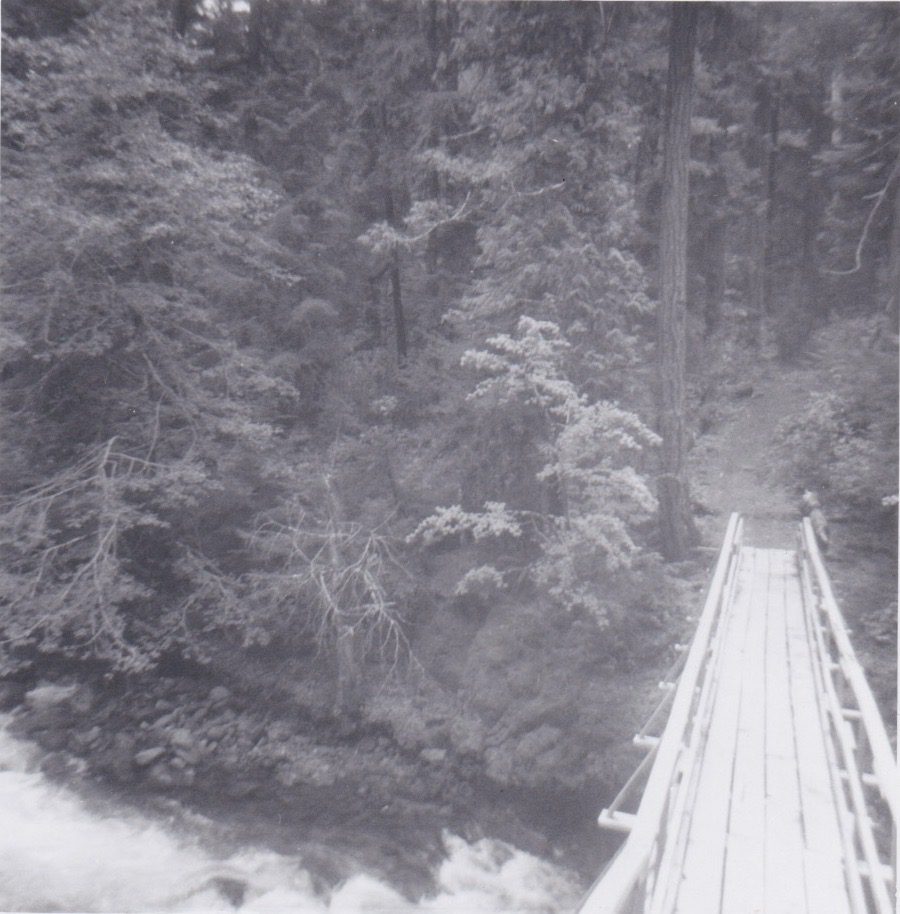 A black and white photo of a wooden bridge over a river.