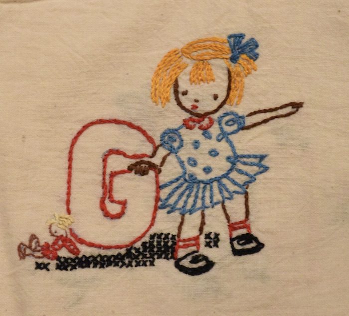 Embroidered letter g with a girl in a dress.