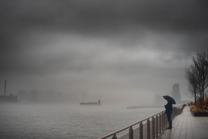 A person looking at the river standing with an umbrella