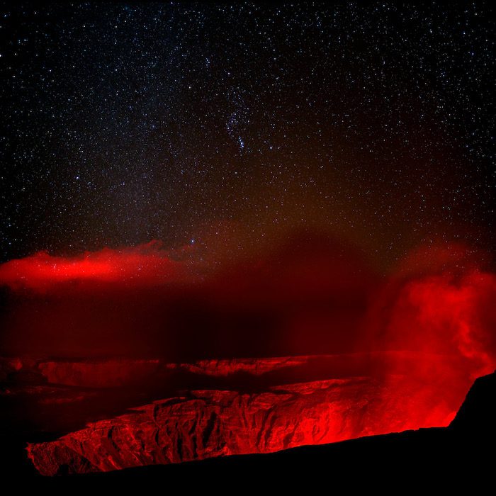 A red lava glows in the night sky above a crater.