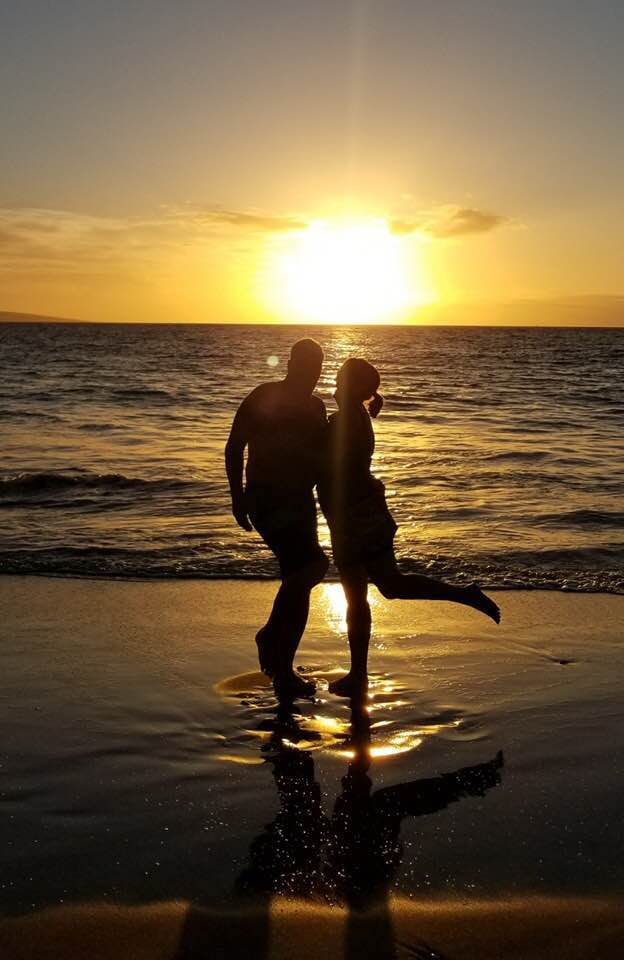 A man and woman standing on the beach at sunset.