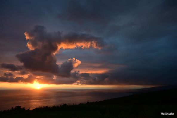 The sun is setting over the ocean with clouds in the background.