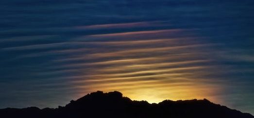 The sun rises over a mountain with clouds in the sky.