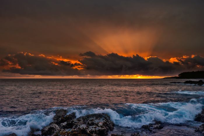 A sunset over the ocean with clouds and waves.