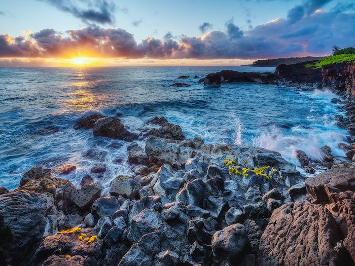 The sun is setting over a rocky shore and ocean.