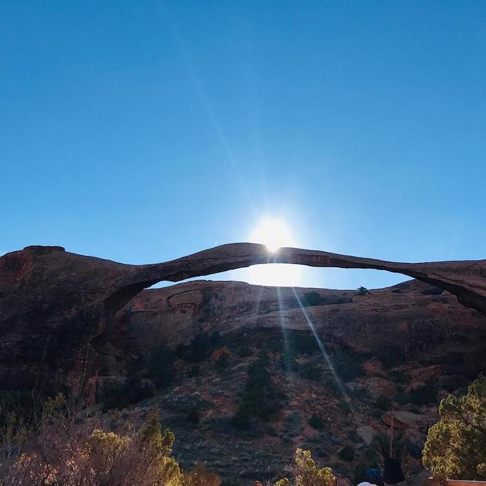 The sun is shining through an arch in the desert.