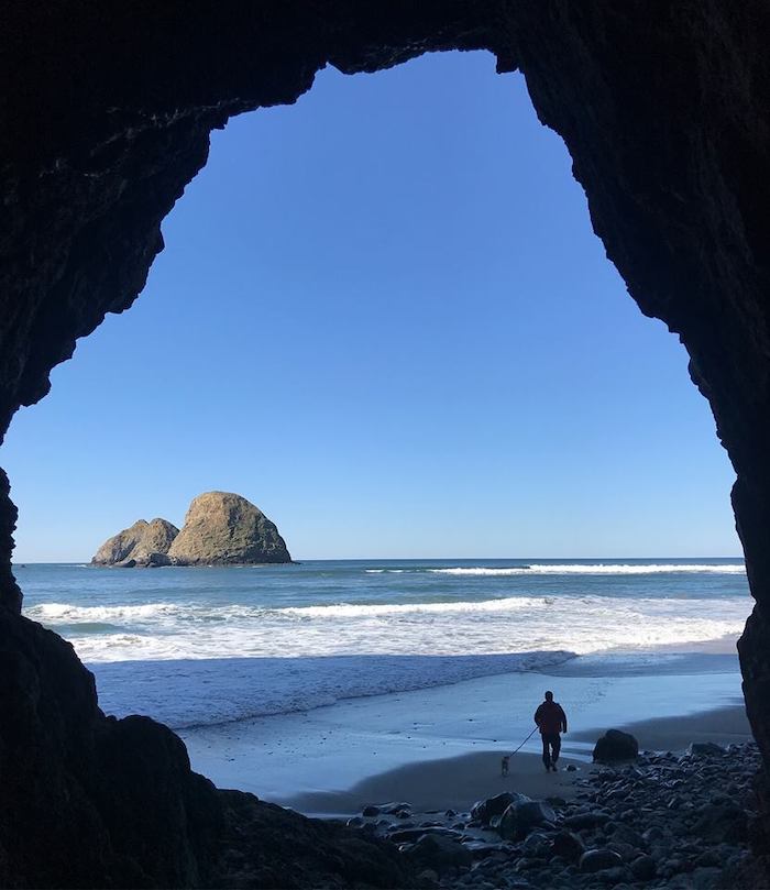 A person is standing in a cave looking at the ocean.