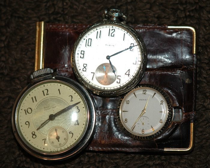 Three pocket watches sitting on top of a brown leather wallet.
