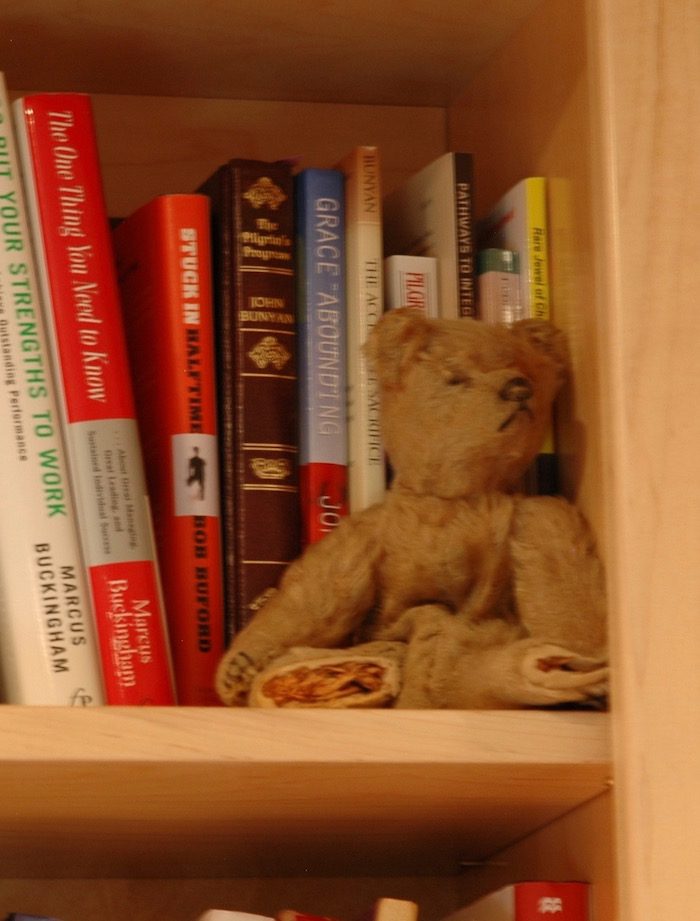 A teddy bear sitting on a book shelf.