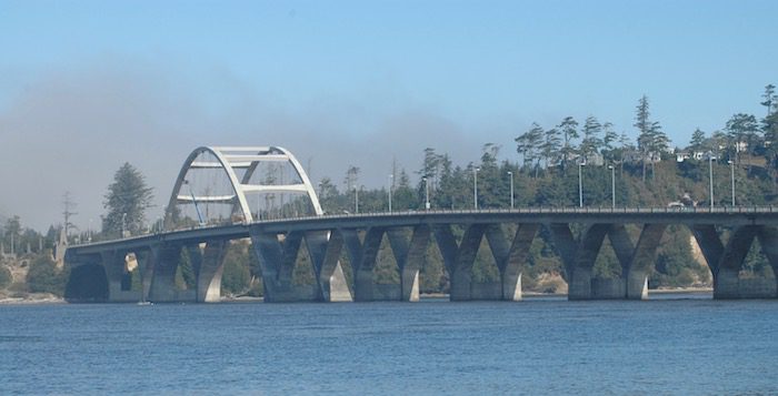 A bridge over a body of water with smoke in the background.