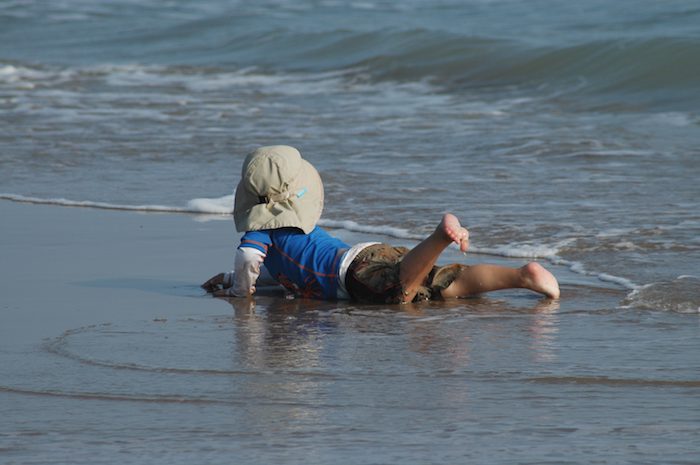 A child laying on the beach with a hat on.