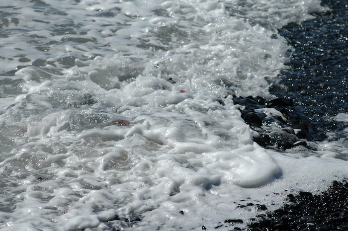 A close up of a black sand beach with waves.