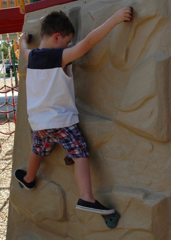 A young boy climbing on a rock wall at a playground.