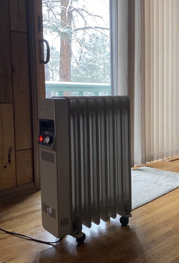 A heater sitting on a wooden floor in front of a window.