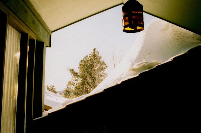 A snow covered porch with a lamp hanging over it.